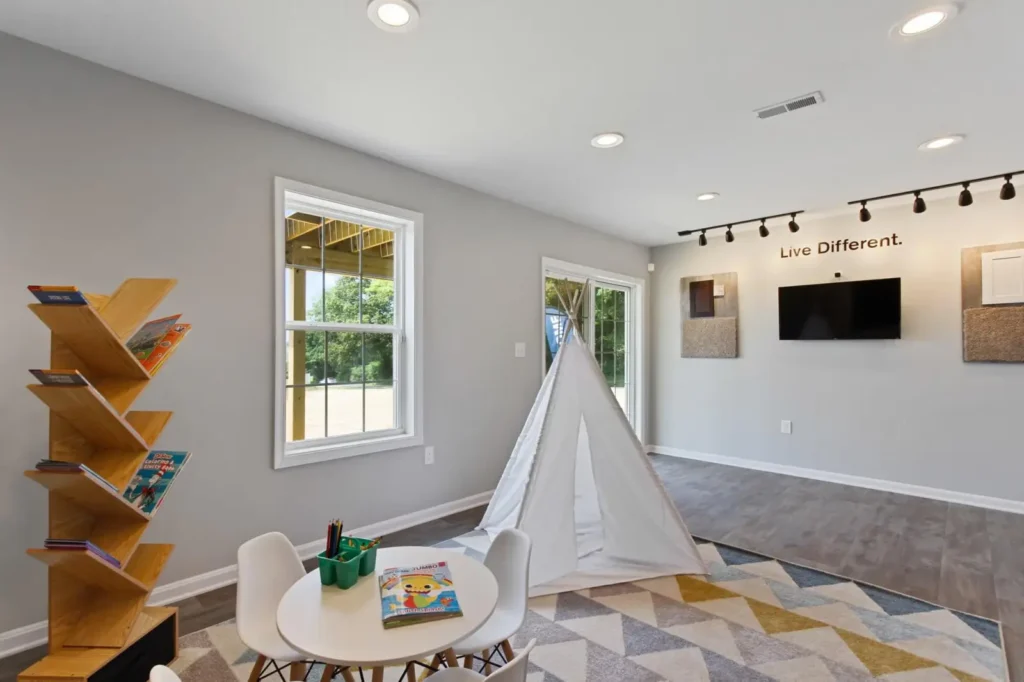 Children's playroom with white teepee, small table and chairs, geometric rug, wooden book rack, and 'Live Different.' wall sign