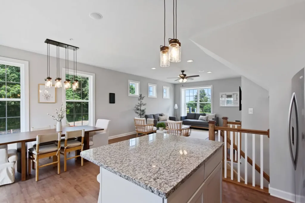 Open-concept kitchen and living area with granite island, pendant lights, dining table, and abundant natural light
