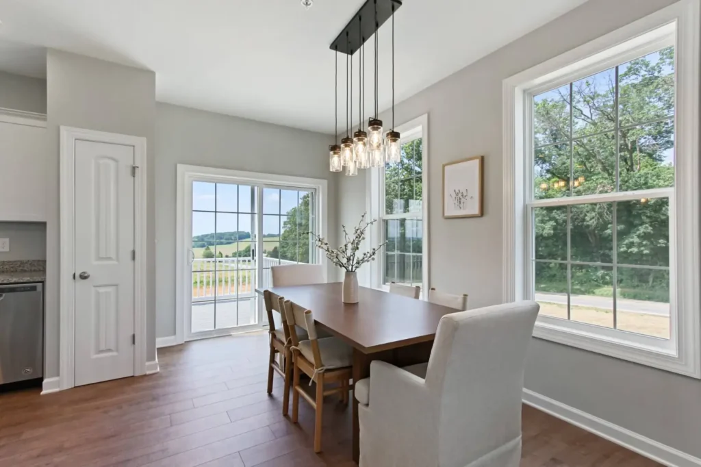 Sunlit dining nook with wooden table, pendant lights, sliding glass door and countryside view
