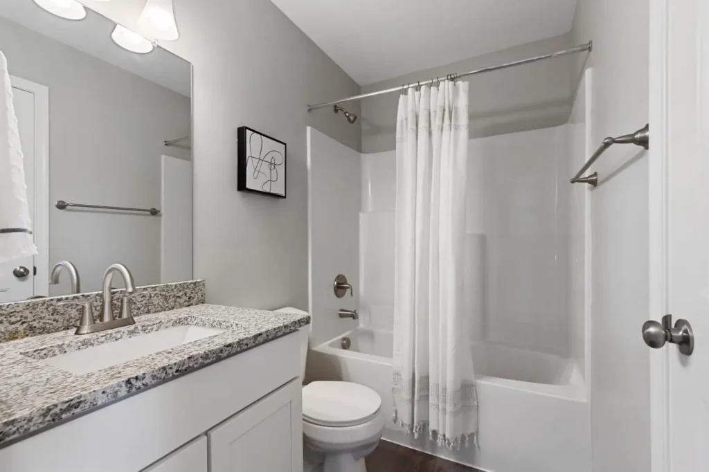 Neutral bathroom with granite vanity, undermount sink, brushed-nickel faucet, toilet, and shower-tub with white curtain