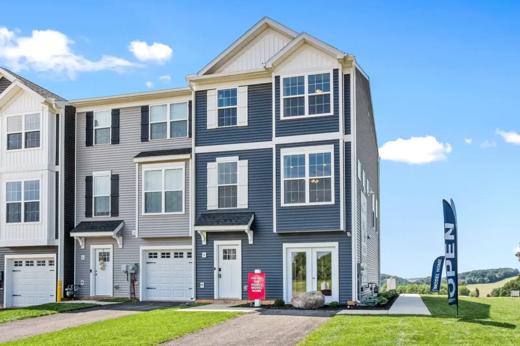 Three-story blue-gray end townhome with garage and an 'OPEN' flag on the lawn