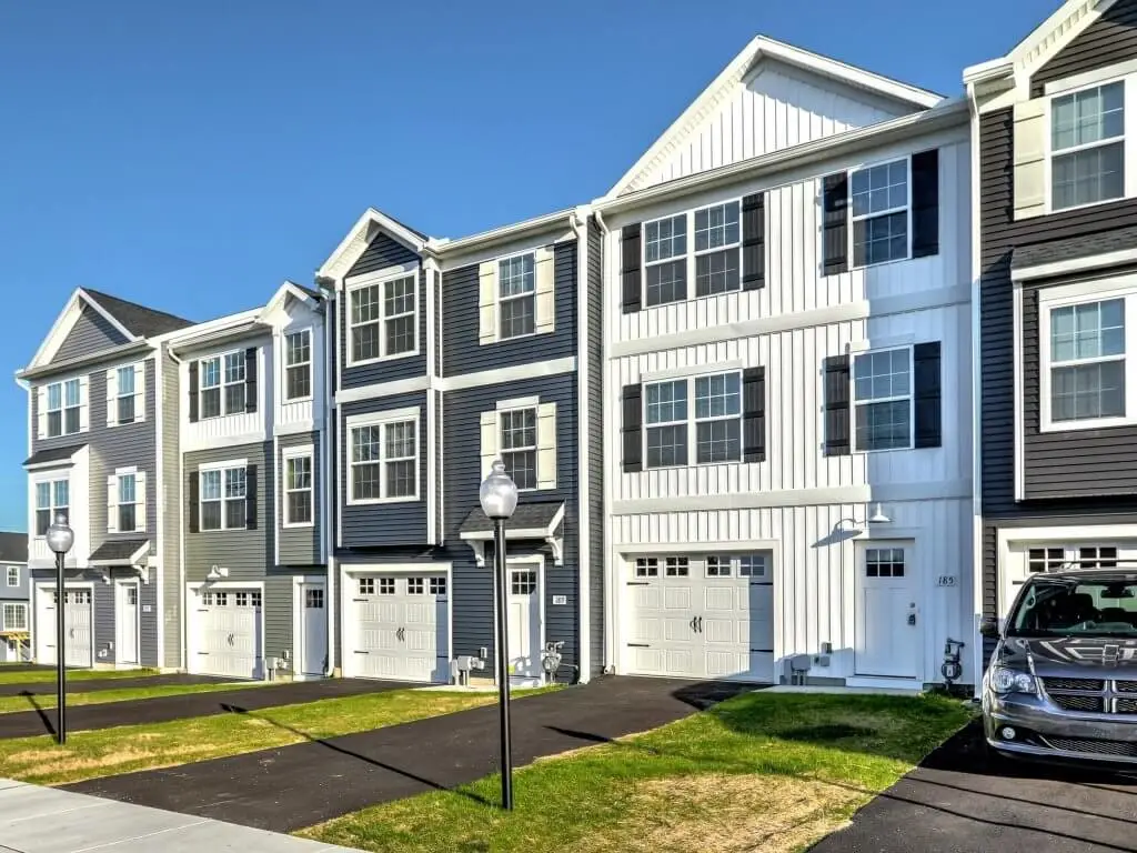 Three-story Burkentine townhomes with attached garages, black shutters, and paved driveways under a clear blue sky