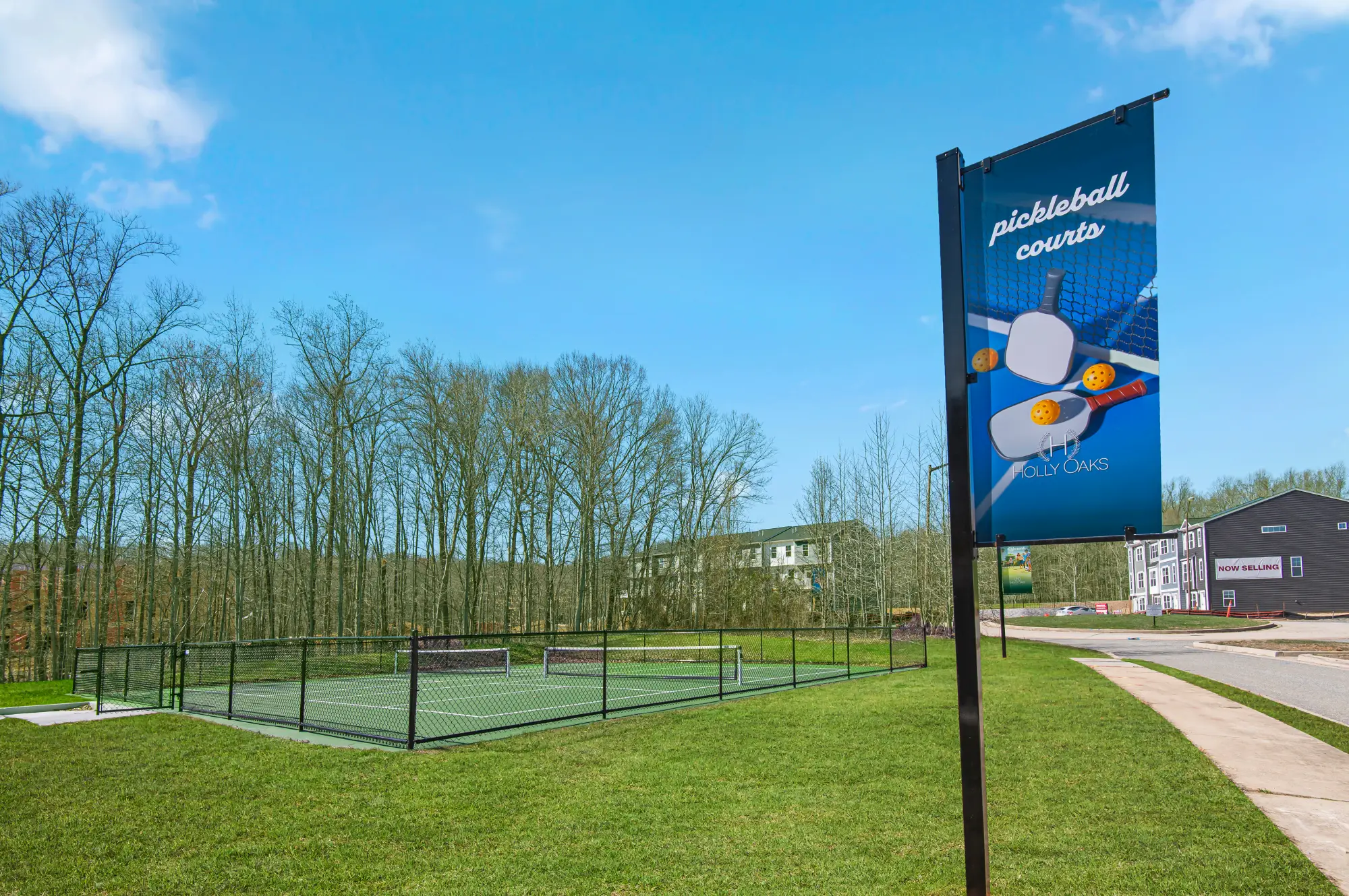 Outdoor pickleball courts and community banner at Holly Oaks with trees and nearby apartments