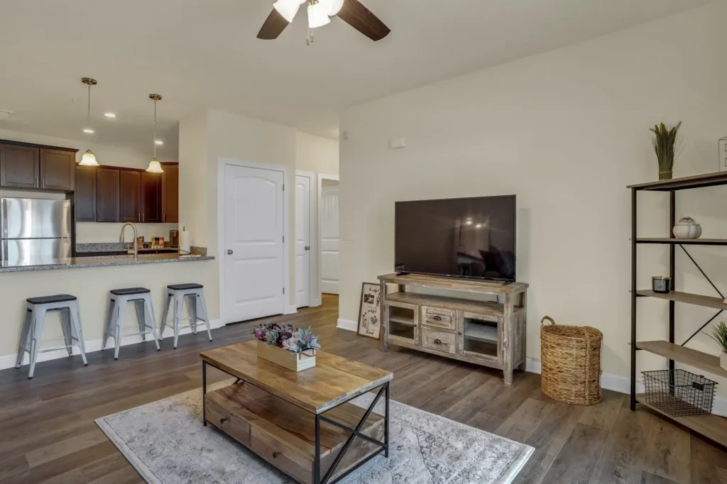 Open-concept living room and kitchen in a rental apartment with bar stools, TV, and wood-tone finishes