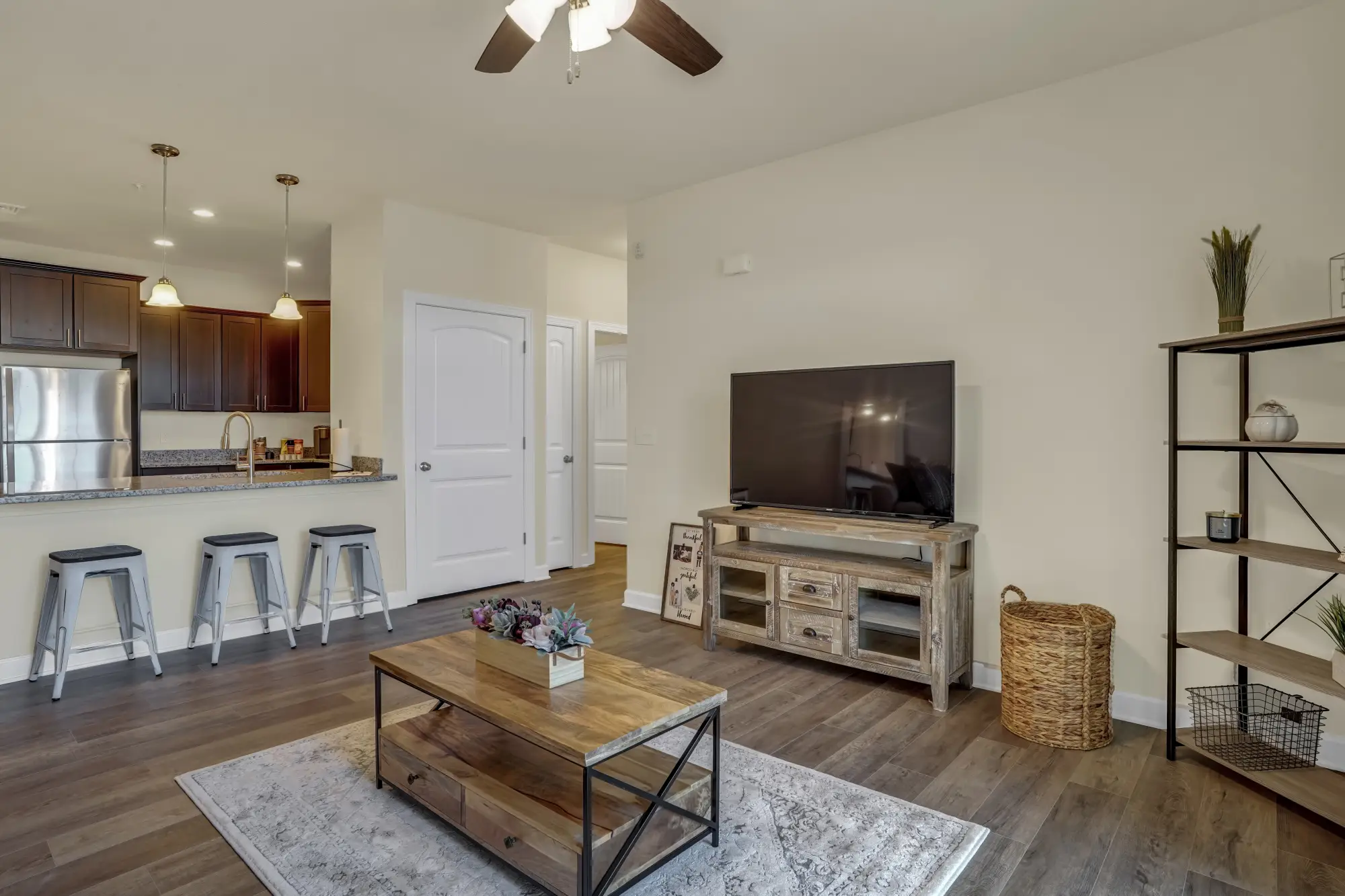 Open-concept living room and kitchen in a rental apartment with bar stools, TV, and wood-tone finishes