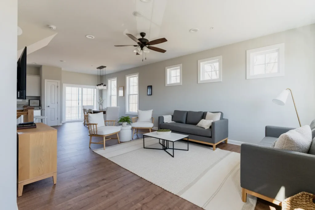 Bright open living room in a new build with gray sofa, white chairs, and ceiling fan
